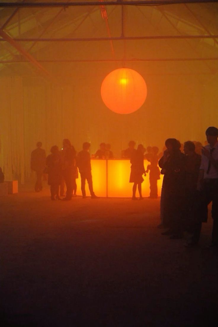 Crowd gathered beneath a luminous orb in a fog-filled hall